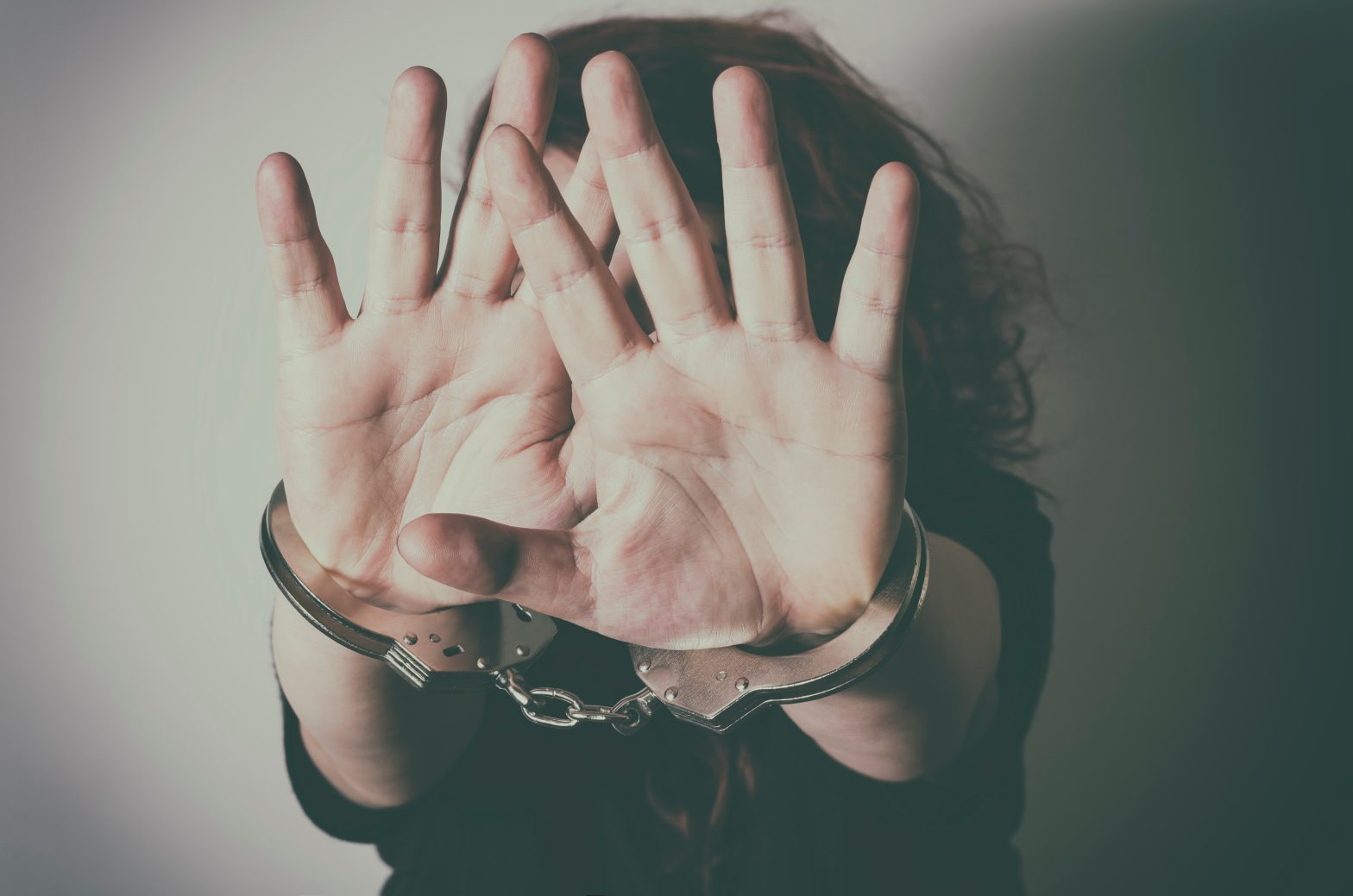 Woman with handcuffs hiding face with her hands.