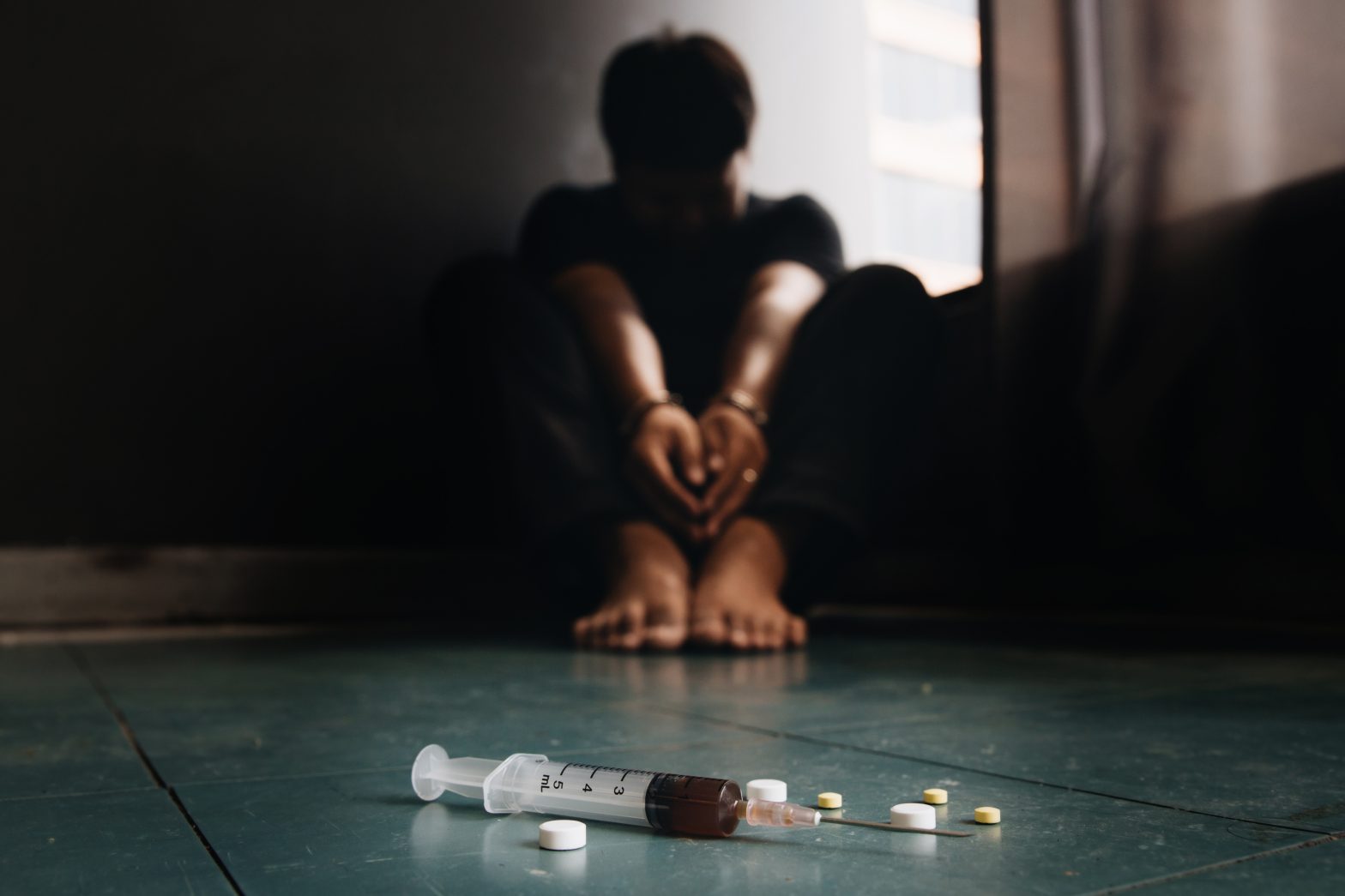 Syringe and drugs with out of focus man sitting on the floor. Drug overdose in prisons, New York prisons.