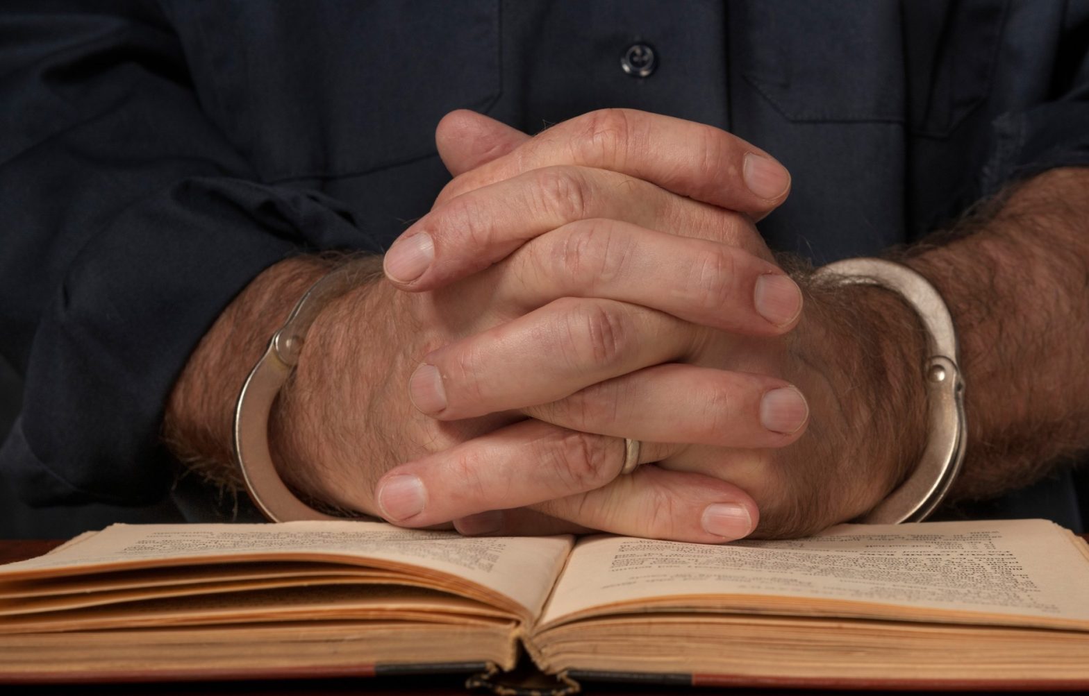 A handcuffed man with clasped hands reads a book about the law. News - NY State Prison Officials lawsuit