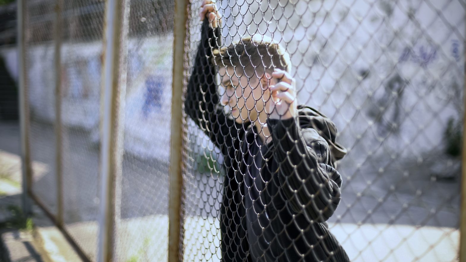 A boy watching through a fence. News - Bernalillo County Juvenile Detention - Advocates Push for Reforms